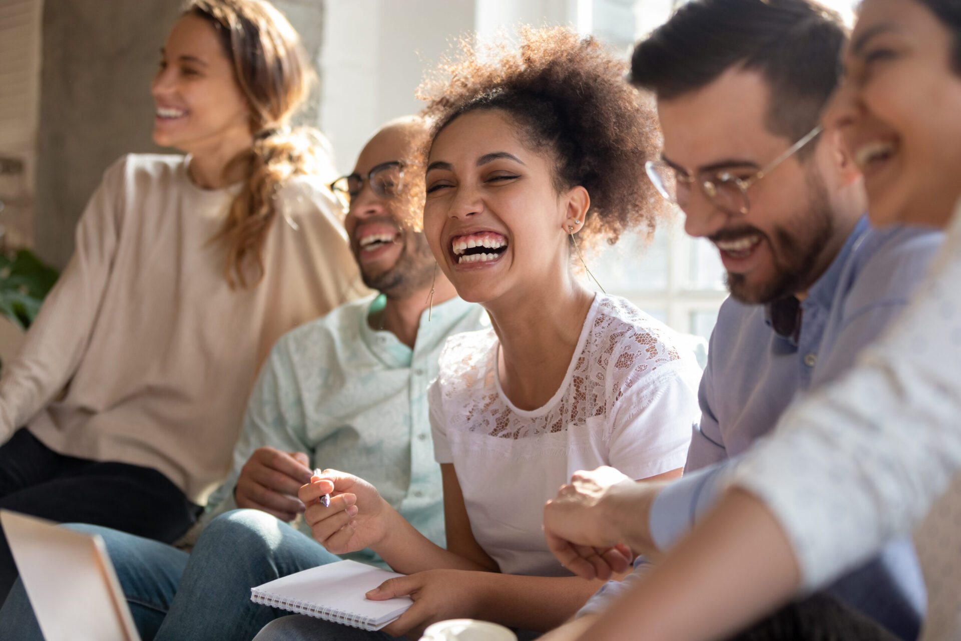 Overjoyed multiracial young people sit in row have fun laughing studying together indoors, happy international diverse students joke chat brainstorm preparing for test making notes learning